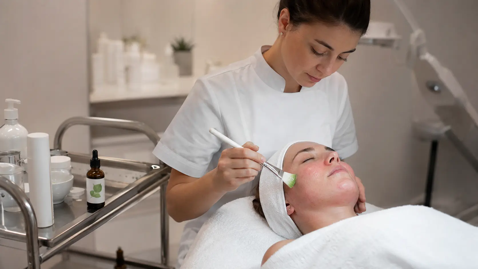 Esthetician applying a centella asiatica serum to a client&rsquo;s face during a post-treatment recovery facial in a softly lit professional treatment room
