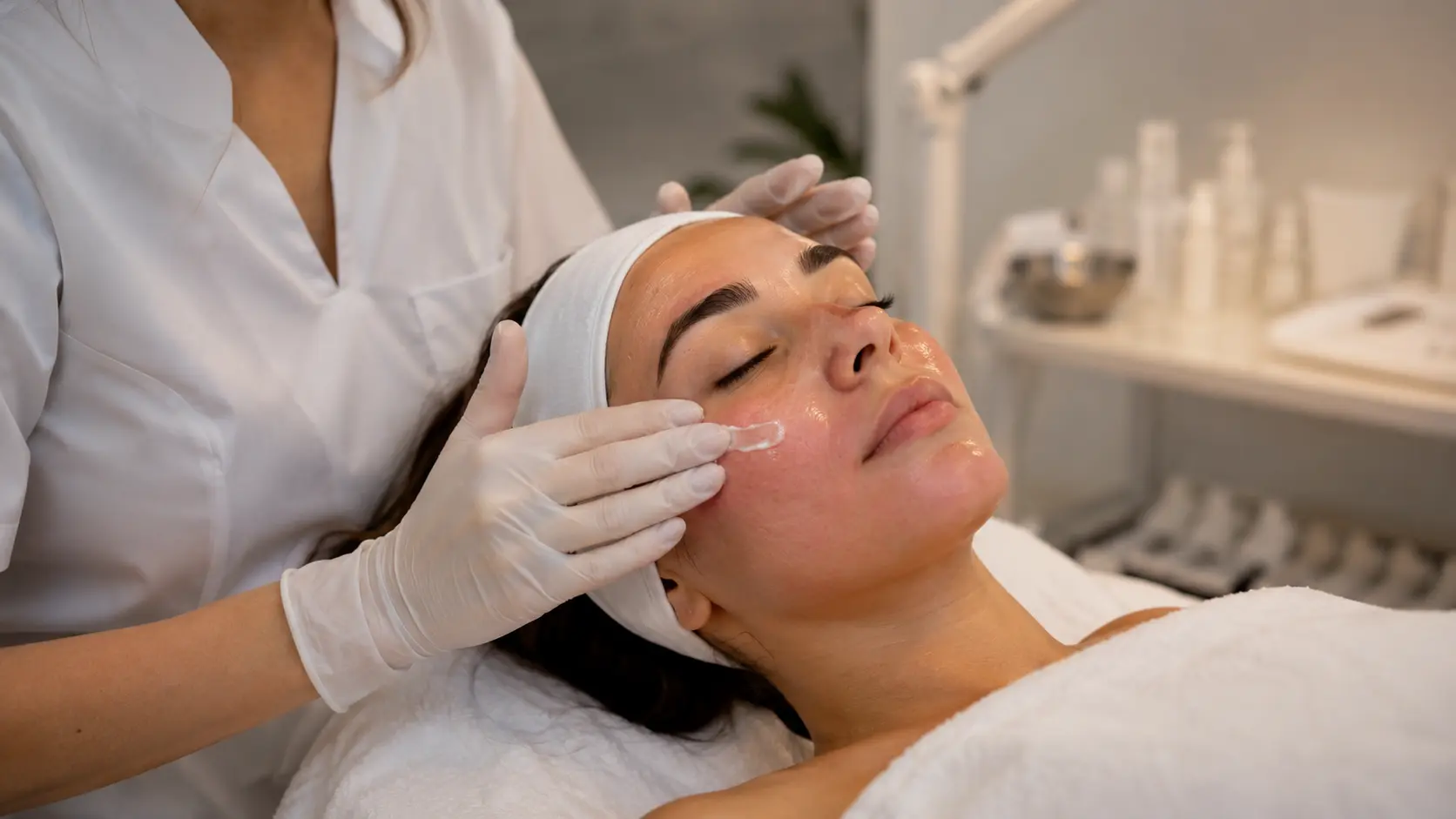 An esthetician applying a barrier repair serum to a client&rsquo;s face in a clean, professional treatment room.